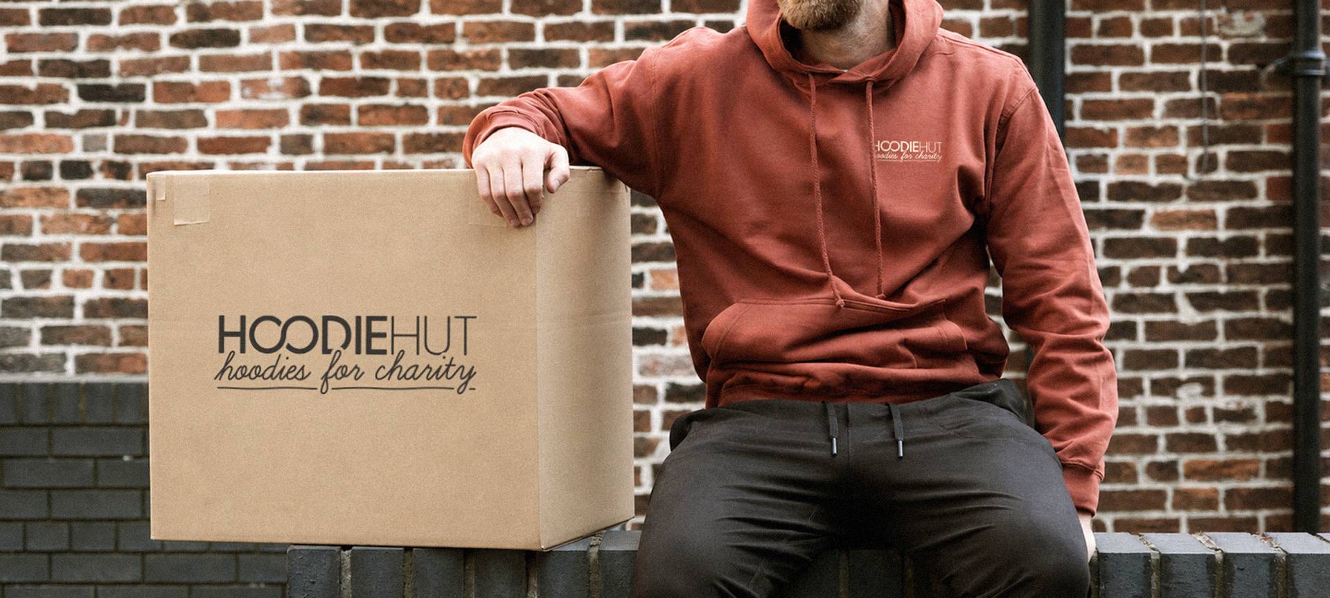 Hoodies for Charity Person wearing a HoodieHut charity hoodie next to a branded donation box
